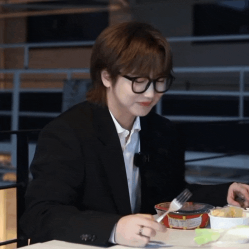 a man in a suit and glasses is sitting at a table with a fork in his hand