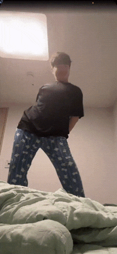 a man in a black shirt and blue pajama pants stands in a bedroom
