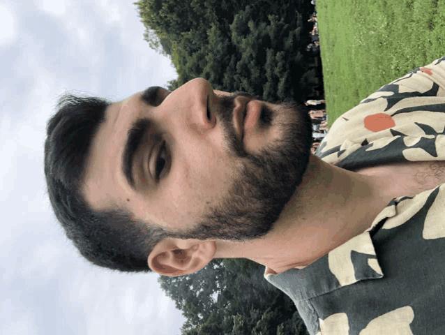 a man with a beard wearing a floral shirt is standing in a field