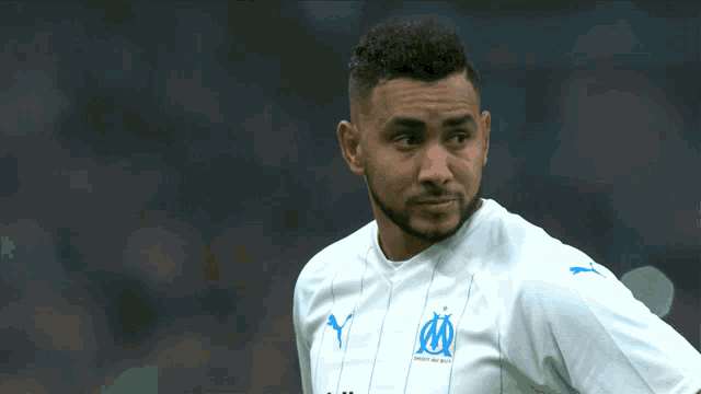 a man with a beard wears a white puma jersey with the letter m on it