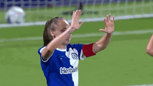 a female soccer player wearing a blue and white shirt with the word herbalife on it