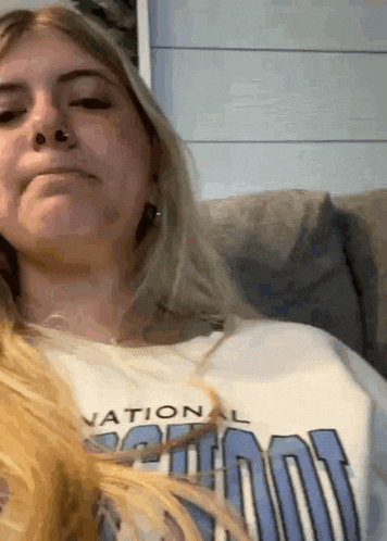 a woman is sitting on a couch wearing a white shirt that says national school .