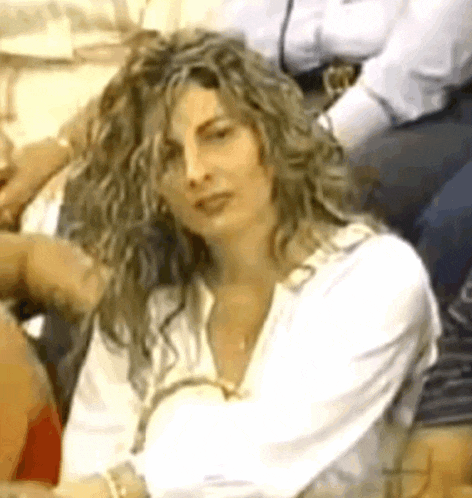 a woman with curly hair is sitting in a crowd of people and looking at the camera .