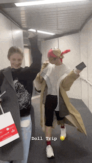 two people are walking down a hallway and one of them is wearing a trench coat .