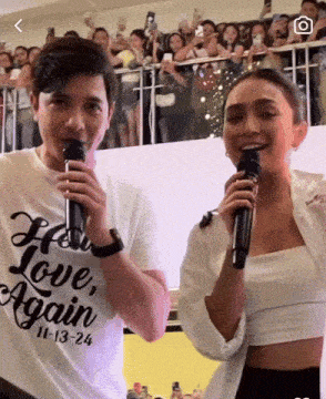 a man and a woman are singing into microphones with the man wearing a shirt that says " how love again "