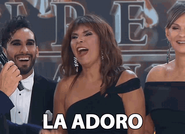 a woman in a black dress says la adoro while a man in a tuxedo holds a microphone