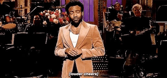a man in a suit says louder cheers while standing on stage
