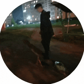 a man in a black jacket is walking a dog in a circle at night