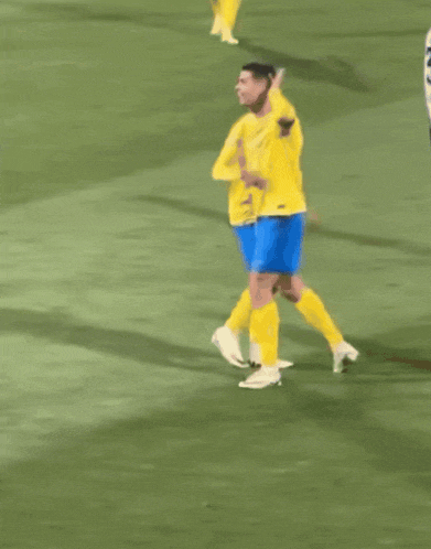 two soccer players wearing yellow jerseys and blue shorts are running on the field
