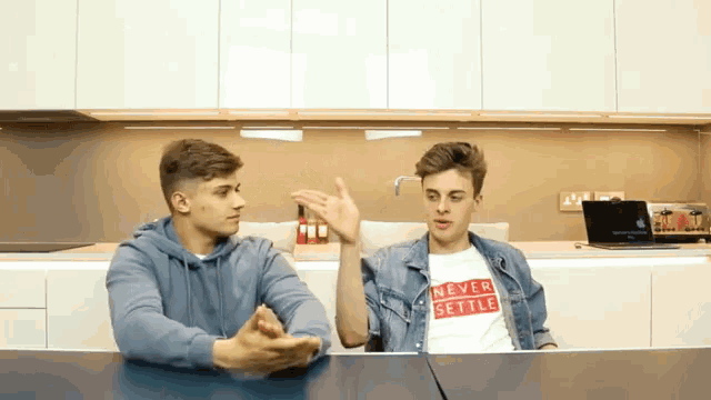 two young men sitting at a table with one wearing a shirt that says " never settle "
