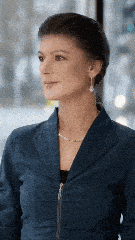 a woman wearing a blue jacket and pearls looks at the camera