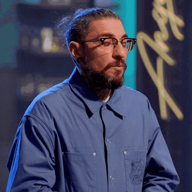 a man wearing glasses and a blue shirt stands in front of a sign that says ' x '