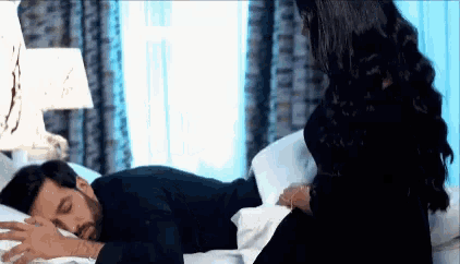 a woman is sitting on a bed next to a man sleeping on it .