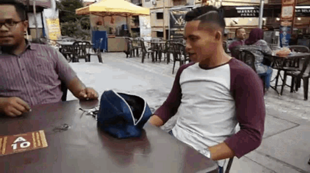 a man is sitting at a table with a bag on it and a sign that says 10 on it .