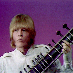 a man in a white shirt is holding a guitar in front of a purple background