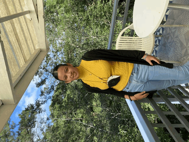 a woman in a yellow sweater is standing on a balcony with trees in the background