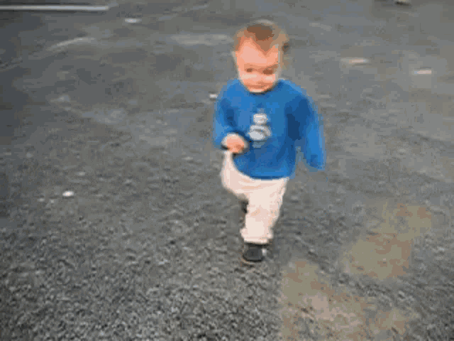 a baby is crawling on the ground wearing a blue shirt .