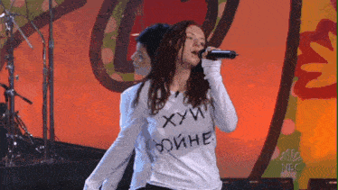 a woman singing into a microphone while wearing a shirt that says " хуй " on it