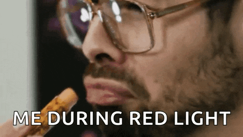 a man with glasses and a beard is eating a snack and says me during red light