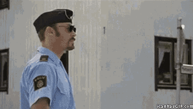 a police officer wearing sunglasses and a hat is standing in a room .