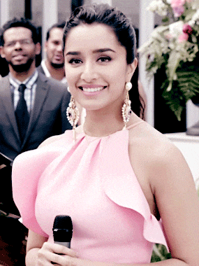 a woman in a pink dress holds a microphone and smiles