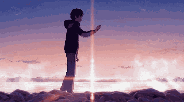 a man in a black jacket stands on a rocky shoreline
