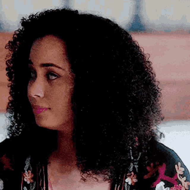 a woman with curly hair is sitting on a bed wearing a floral kimono .