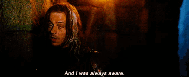 a man with long hair says " and i was always aware " in a dark room