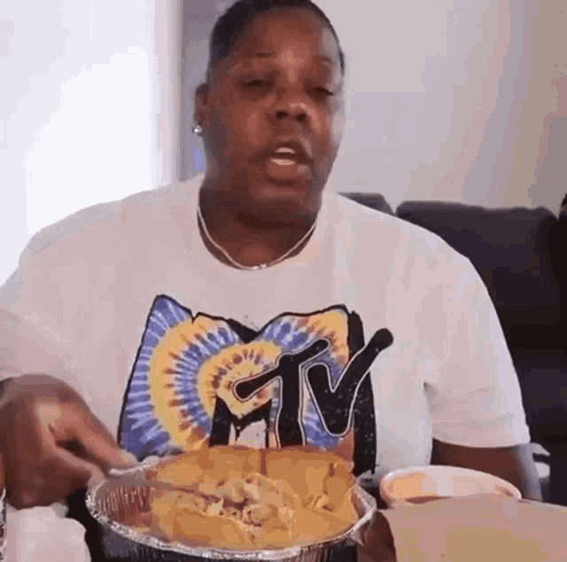 a woman wearing a tie dye shirt is eating a casserole dish of nachos .