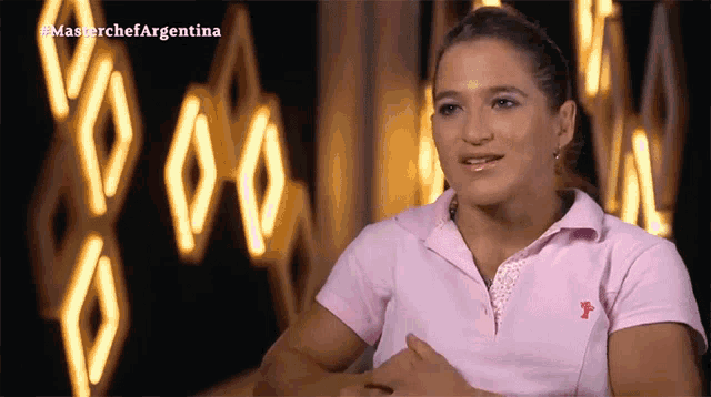 a woman in a pink polo shirt is sitting in front of a sign that says masterchef argentina on it