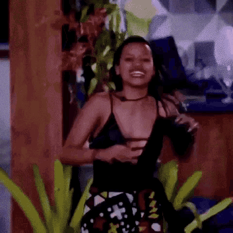 a woman in a black tank top is standing in front of a wooden wall and smiling .