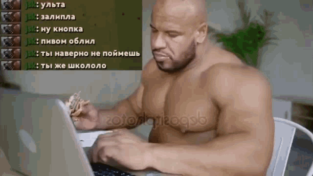 a shirtless man sits in front of a laptop with russian text on the screen behind him including the letters j and k