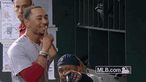 a man in a baseball uniform holds his finger to his lips in a locker room with mlb.com in the corner