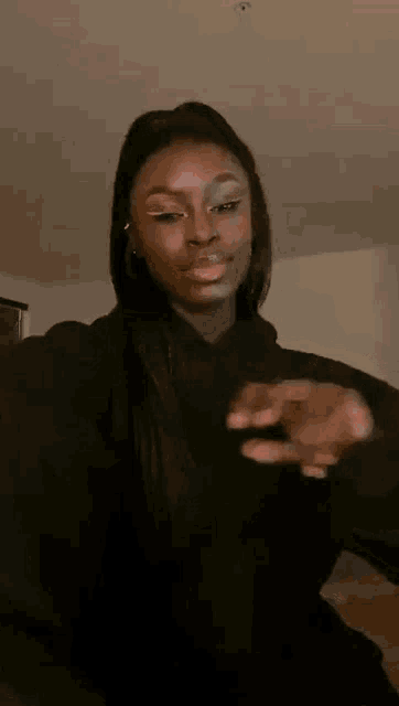a woman in a black hoodie is making a funny face while holding her hands together .