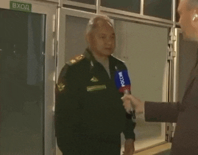 a man in a military uniform is talking into a microphone while another man holds his hand out towards him .