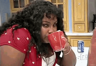 a woman is drinking from a red cup while sitting at a table in a kitchen .