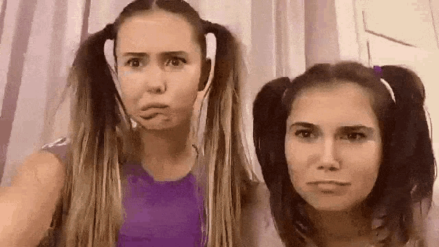 two girls with pigtails are making funny faces and looking at the camera .