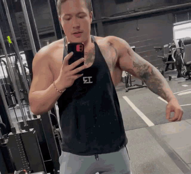 a man taking a picture of himself in a gym wearing a tank top with the letter i on it
