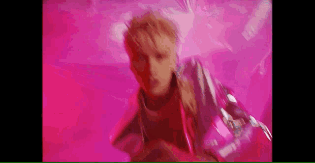 a blurry picture of a man in a pink jacket dancing in a pink room .