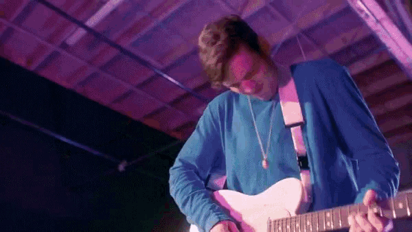 a man in a blue shirt is playing a pink guitar on stage .