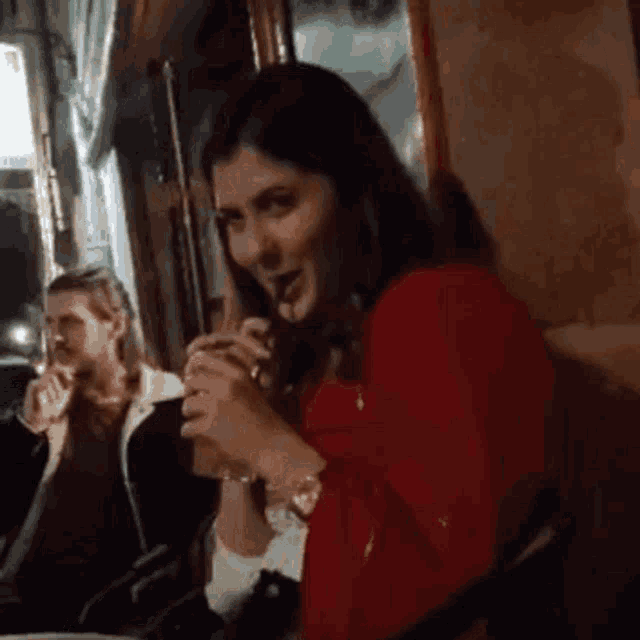 a woman in a red dress is eating a hamburger in a restaurant while a man looks on .