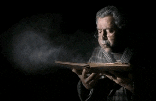 a man with glasses is reading a book in the dark