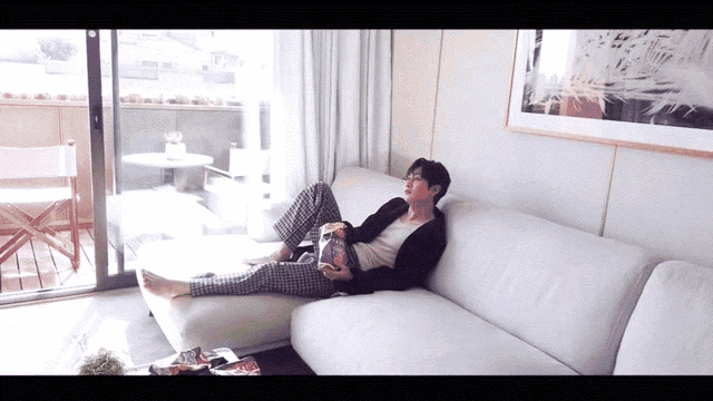 a man laying on a white couch reading a magazine