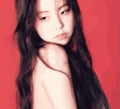 a woman with long hair is standing in front of a red background and looking over her shoulder .
