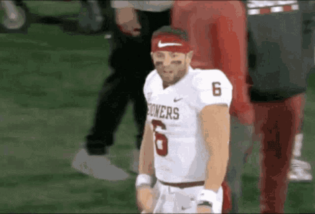 a football player wearing a headband and a jersey with the number 6 on it is standing on the field .