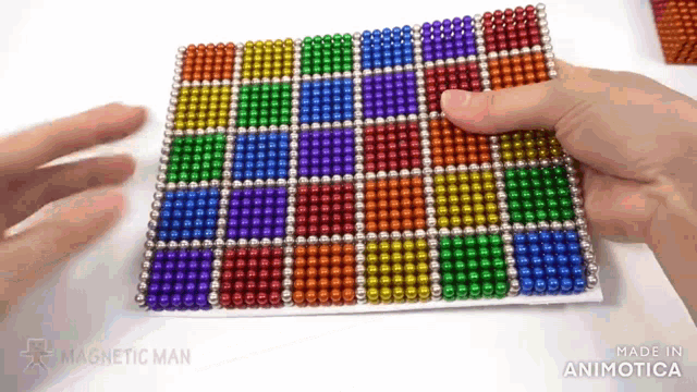 a person is playing with a rainbow of magnetic beads on a white surface .