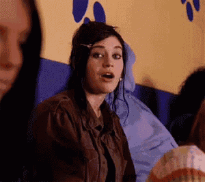 a woman in a brown jacket is sitting in front of a yellow wall with blue paw prints .