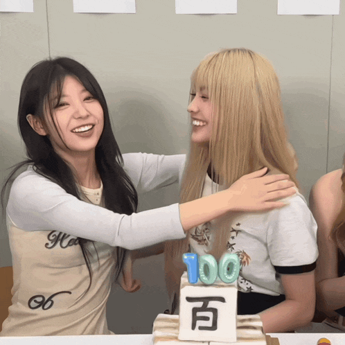 two girls hugging in front of a cake that says 100 on it