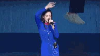 a woman in a blue jumpsuit is singing into a microphone .