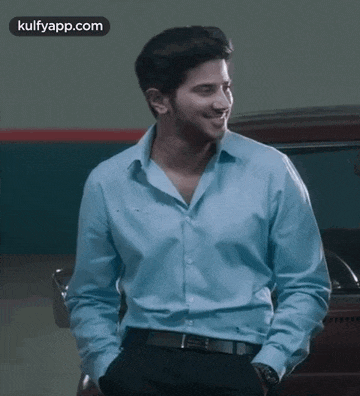 a man wearing a blue shirt and black pants is smiling with his hands in his pockets